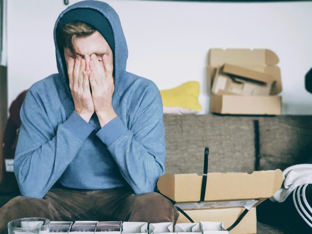 Stressed student in a blue hoodie is covering his face with both of his hands
